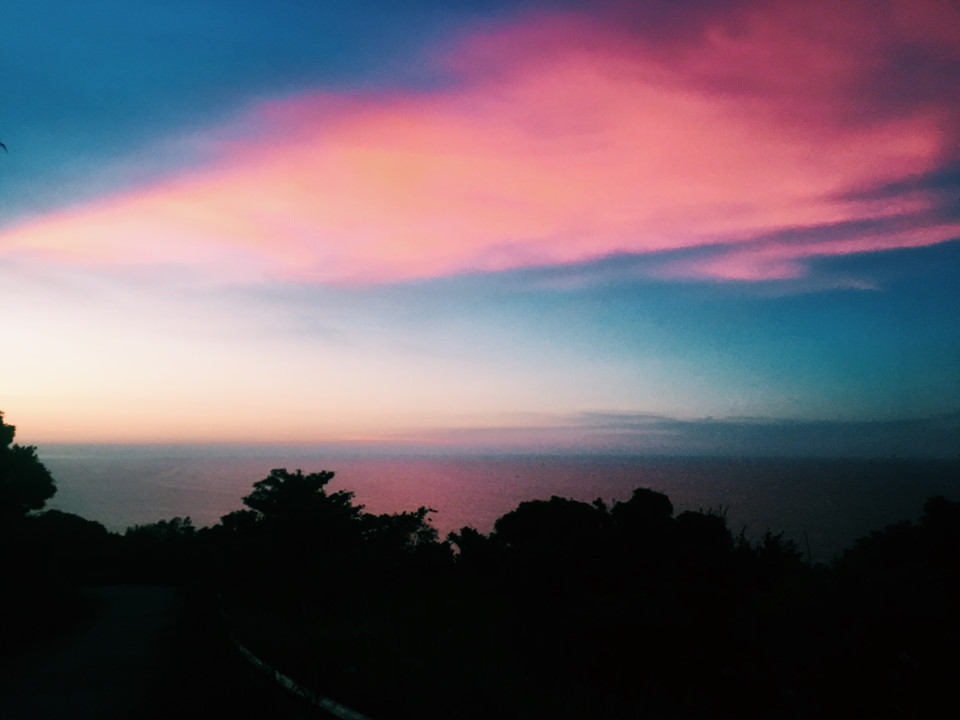 Hoàng hôn nhuộm hồng cả bầu trời, in bóng xuống mặt biển.