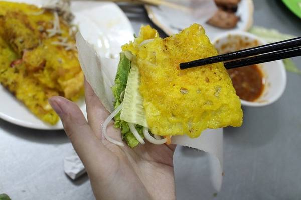 Bánh được dọn ra đĩa nóng hổi, cắt đôi miếng bánh cho dễ cuốn, bên cạnh là đĩa rau sống, đu đủ chua và dưa leo cuốn kèm bánh tráng mỏng.